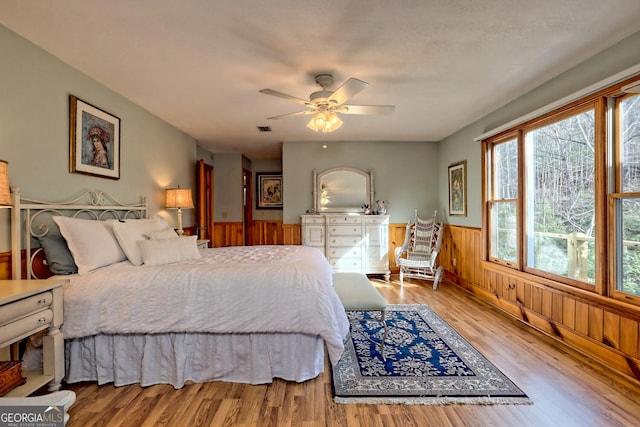 bedroom with ceiling fan, wood walls, and wood-type flooring