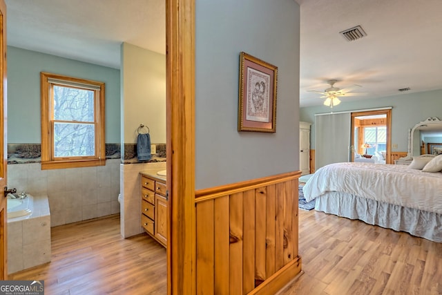 bedroom with tile walls, light hardwood / wood-style flooring, multiple windows, and ceiling fan