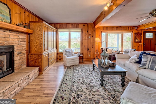 living room featuring ceiling fan, ornamental molding, a stone fireplace, wooden walls, and light hardwood / wood-style floors