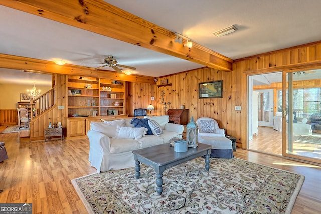 living room with ceiling fan with notable chandelier, light wood-type flooring, and wood walls