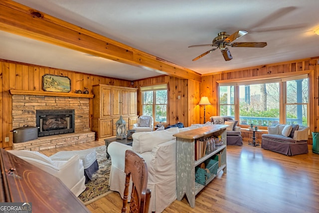 living room featuring ceiling fan, a stone fireplace, light wood-type flooring, and wood walls