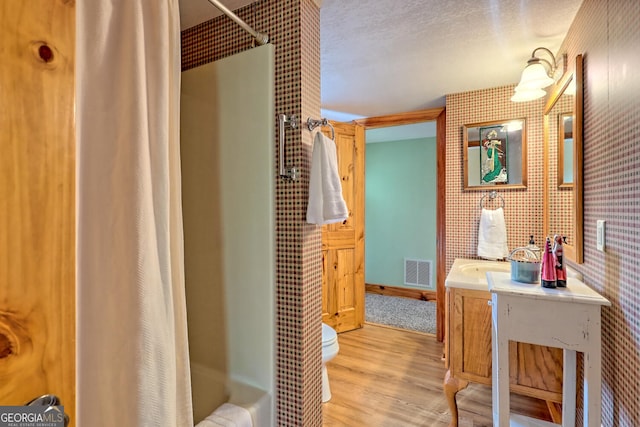 full bathroom featuring vanity, wood-type flooring, a textured ceiling, toilet, and shower / tub combo with curtain