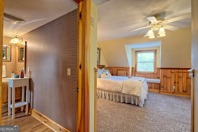 bedroom with a textured ceiling, wood-type flooring, wooden walls, and ceiling fan