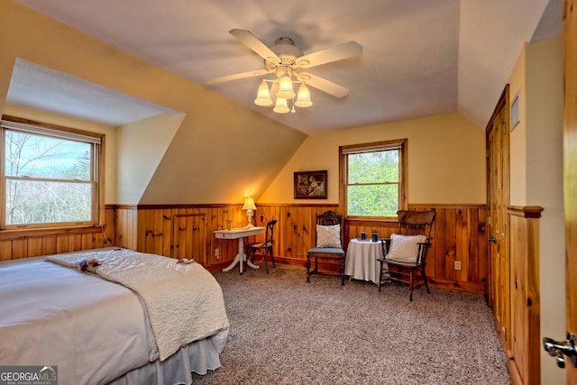 bedroom with ceiling fan, wood walls, vaulted ceiling, and carpet flooring