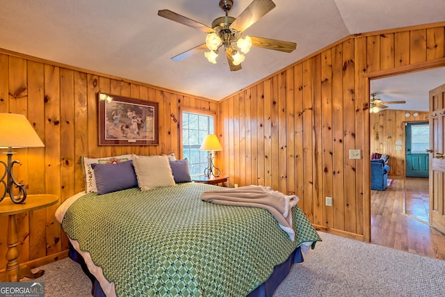 bedroom with wood-type flooring, lofted ceiling, wood walls, and ceiling fan