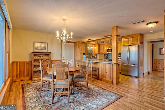 dining room featuring wooden walls, an inviting chandelier, light wood-type flooring, and a textured ceiling