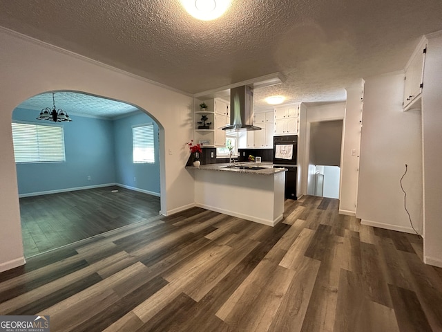 kitchen featuring a notable chandelier, wall chimney range hood, a textured ceiling, white cabinets, and dark hardwood / wood-style flooring