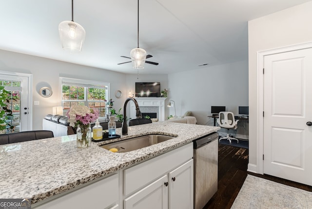 kitchen featuring stainless steel dishwasher, ceiling fan, dark wood-type flooring, sink, and light stone counters