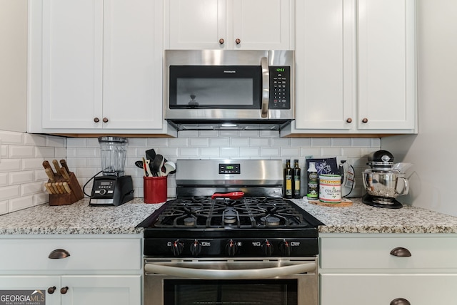 kitchen with light stone countertops, tasteful backsplash, appliances with stainless steel finishes, and white cabinetry