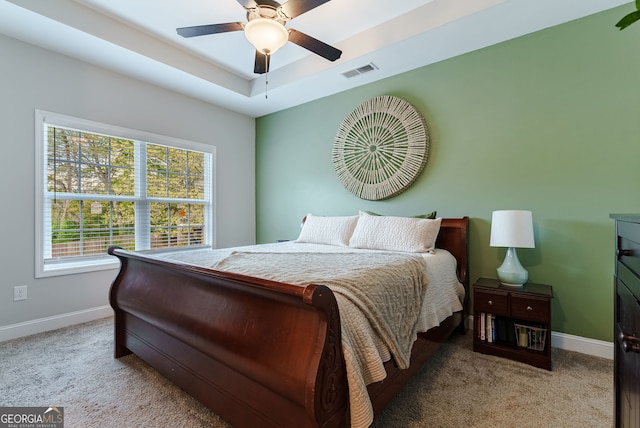 carpeted bedroom with ceiling fan and a raised ceiling