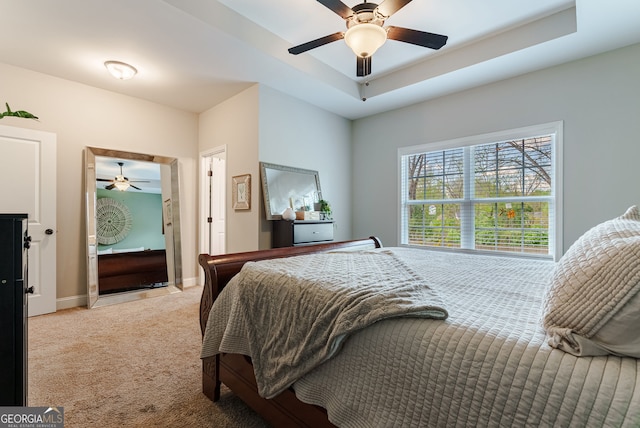 carpeted bedroom with a raised ceiling and ceiling fan