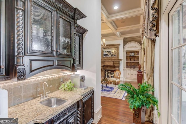 kitchen with coffered ceiling, a chandelier, light stone counters, dark hardwood / wood-style floors, and sink