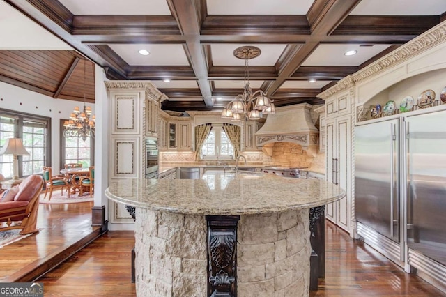 kitchen with decorative light fixtures, an inviting chandelier, dark wood-type flooring, custom range hood, and light stone countertops