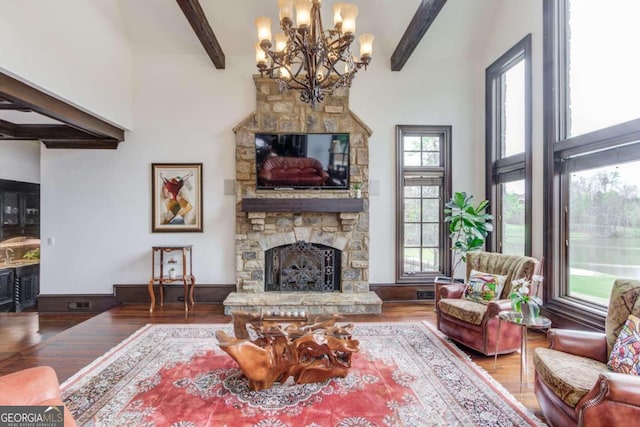 living room with a wealth of natural light, a stone fireplace, an inviting chandelier, and beamed ceiling