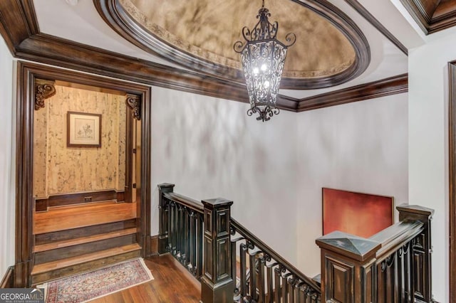 staircase featuring dark hardwood / wood-style flooring, crown molding, a notable chandelier, and a raised ceiling