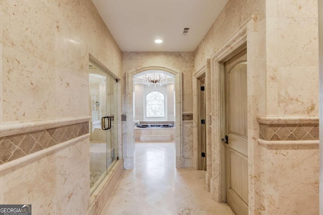 hall featuring a notable chandelier, light tile flooring, and tile walls