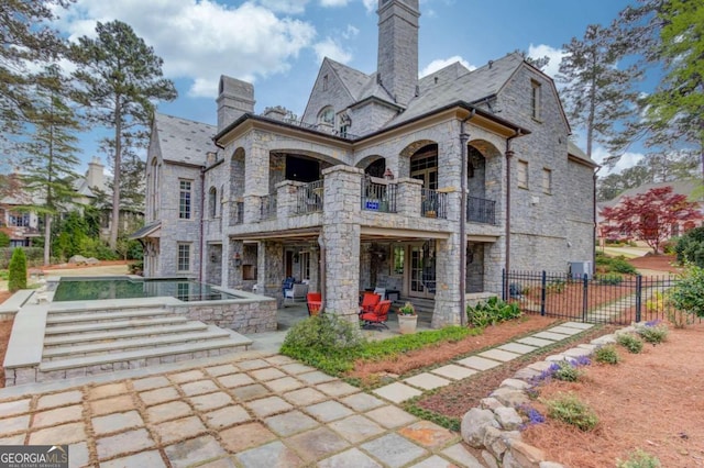 rear view of house with a balcony, a fenced in pool, and a patio area