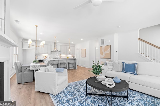 living area featuring stairs, light wood finished floors, recessed lighting, visible vents, and ceiling fan with notable chandelier