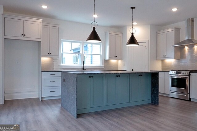 kitchen featuring hardwood / wood-style flooring, tasteful backsplash, stainless steel stove, and wall chimney exhaust hood