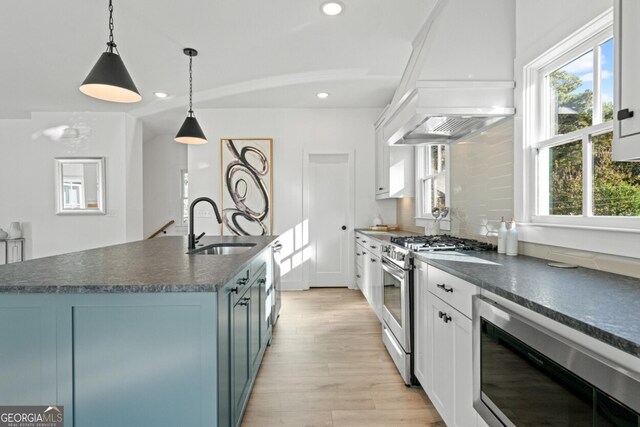 kitchen with light hardwood / wood-style flooring, premium range hood, sink, white cabinetry, and appliances with stainless steel finishes