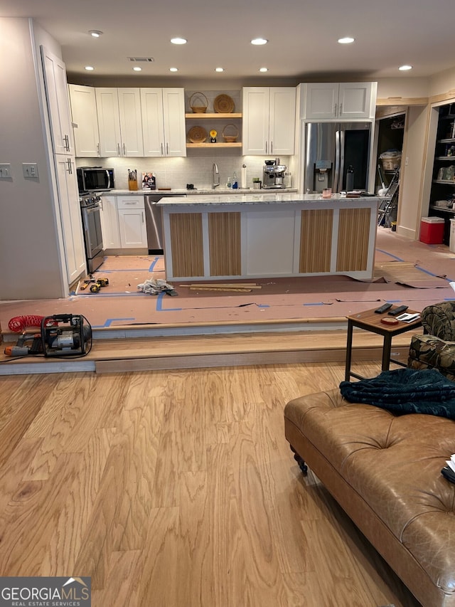 kitchen featuring a kitchen breakfast bar, tasteful backsplash, stainless steel appliances, a kitchen island, and white cabinetry