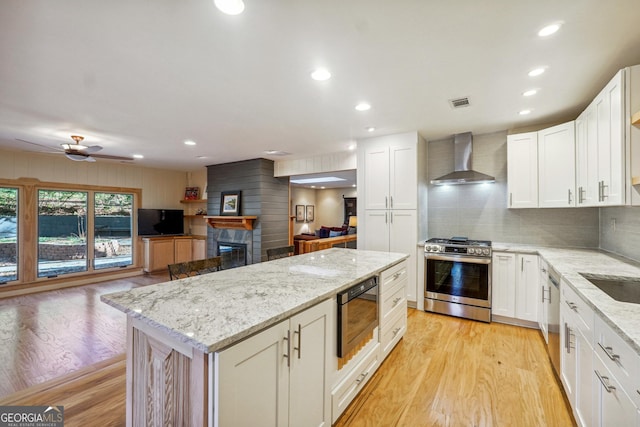 kitchen featuring wall chimney exhaust hood, light hardwood / wood-style floors, built in microwave, and stainless steel gas range