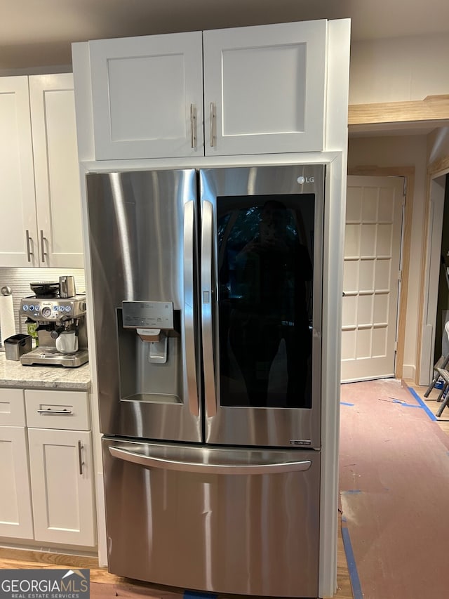 kitchen with stainless steel fridge with ice dispenser, light hardwood / wood-style flooring, white cabinetry, and light stone counters