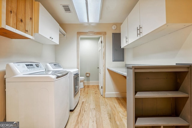 clothes washing area with separate washer and dryer, light hardwood / wood-style flooring, cabinets, and electric panel