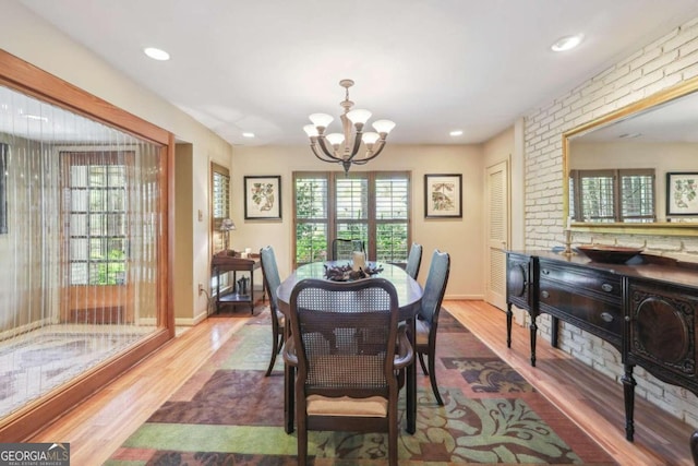 dining space featuring a chandelier, wood-type flooring, a wealth of natural light, and brick wall