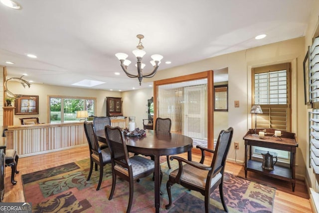 dining room with light wood-type flooring, a skylight, and a notable chandelier