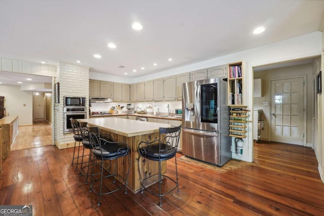 kitchen with sink, a breakfast bar area, dark hardwood / wood-style floors, a kitchen island, and stainless steel appliances