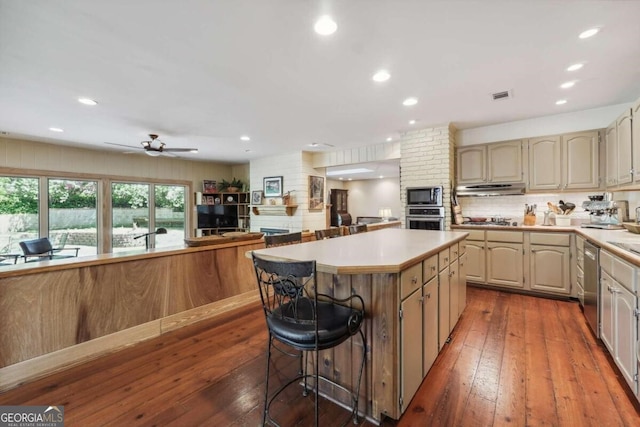 kitchen featuring hardwood / wood-style floors, a breakfast bar, a center island, ceiling fan, and stainless steel appliances