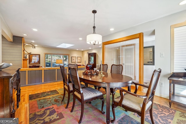 dining space with a skylight, an inviting chandelier, and hardwood / wood-style flooring