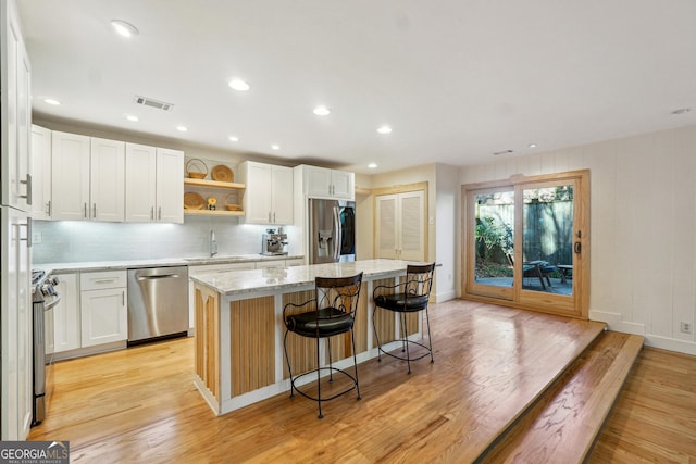 kitchen with white cabinets, a kitchen island, light wood-type flooring, and stainless steel appliances