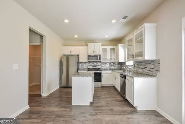 kitchen with appliances with stainless steel finishes, dark hardwood / wood-style flooring, a center island, and light stone countertops