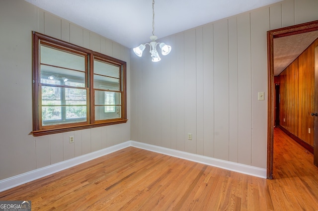 empty room featuring wood walls, a notable chandelier, and light wood-type flooring