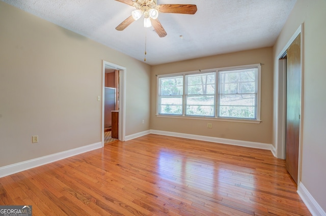 empty room with ceiling fan, a textured ceiling, and light wood-type flooring