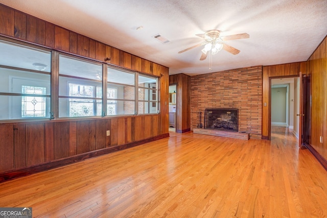 unfurnished living room featuring light hardwood / wood-style flooring, ceiling fan, a large fireplace, and wooden walls