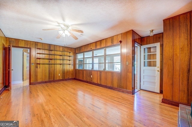 unfurnished room with wooden walls, light hardwood / wood-style flooring, and a textured ceiling