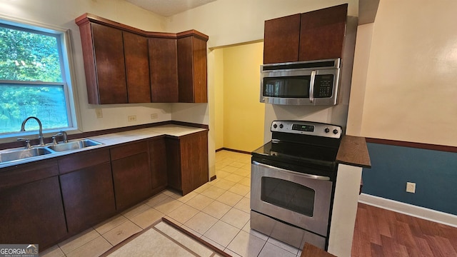 kitchen featuring dark brown cabinetry, sink, stainless steel appliances, and light tile floors