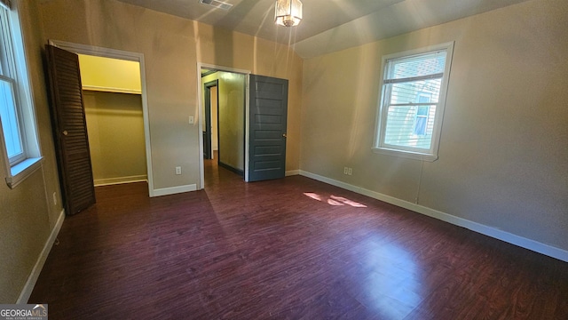 unfurnished bedroom featuring dark wood-type flooring, a spacious closet, and a closet