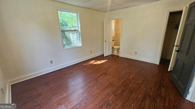 unfurnished bedroom featuring dark hardwood / wood-style flooring, ensuite bathroom, and a paneled ceiling