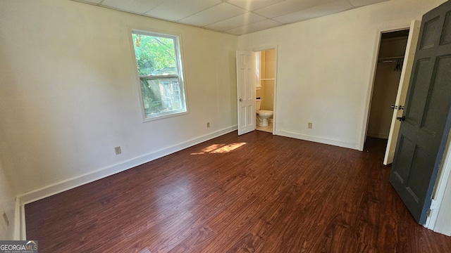 unfurnished bedroom featuring ensuite bath, dark wood-type flooring, a paneled ceiling, and a closet