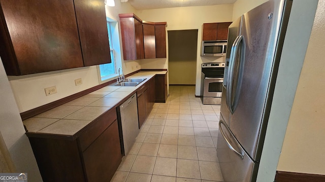 kitchen featuring appliances with stainless steel finishes, light tile flooring, dark brown cabinetry, tile countertops, and sink