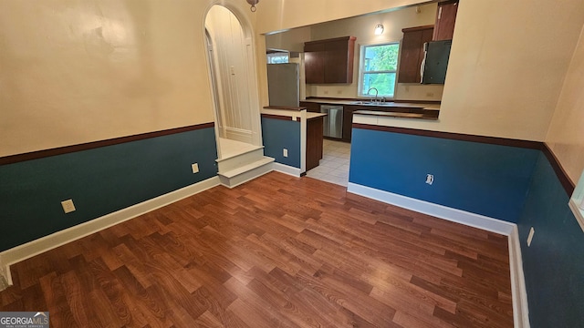 kitchen featuring dark brown cabinetry, appliances with stainless steel finishes, sink, light wood-type flooring, and kitchen peninsula