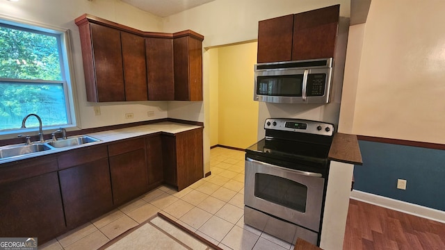 kitchen featuring appliances with stainless steel finishes, dark brown cabinetry, sink, and light tile floors