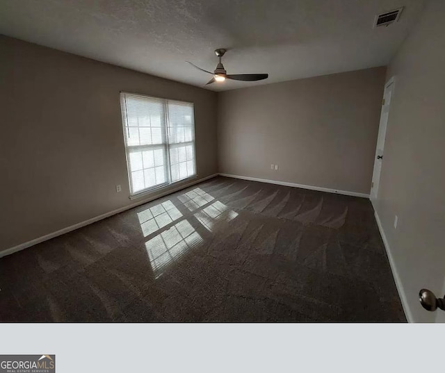 empty room with a textured ceiling, ceiling fan, and dark colored carpet