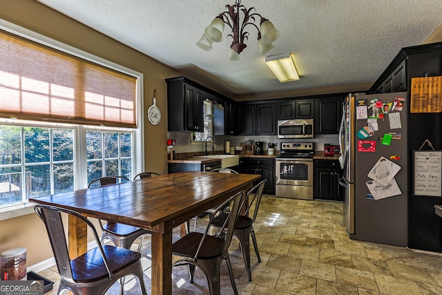 kitchen with light tile floors, stainless steel appliances, backsplash, sink, and a notable chandelier