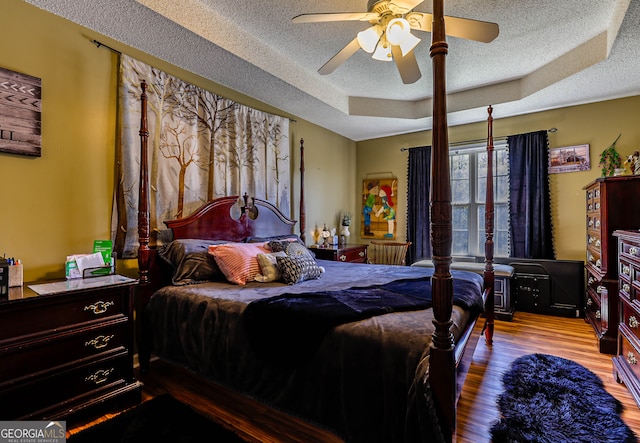 bedroom featuring ceiling fan, a raised ceiling, hardwood / wood-style flooring, and a textured ceiling