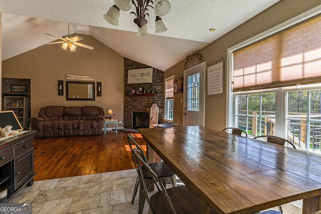 tiled dining room featuring lofted ceiling, ceiling fan, a stone fireplace, and a textured ceiling